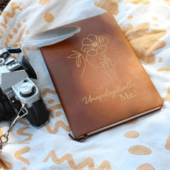 Havijo Unapologetically Me leather journal with textured brown cover and metal clasp, resting on a wooden surface.